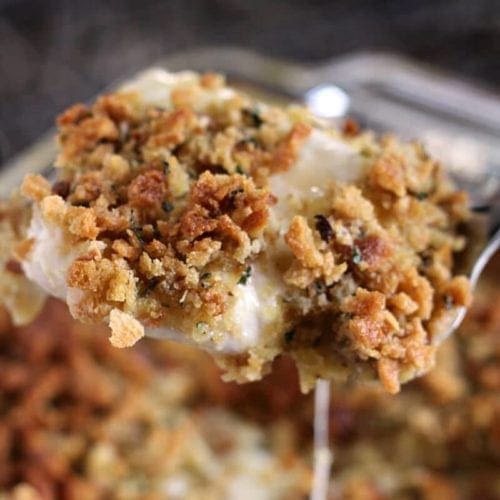 A spatula lifting a cheesy chicken stuffing casserole piece out of a baking dish