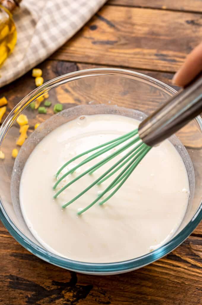 Milk and flour being whisked in glass bowl