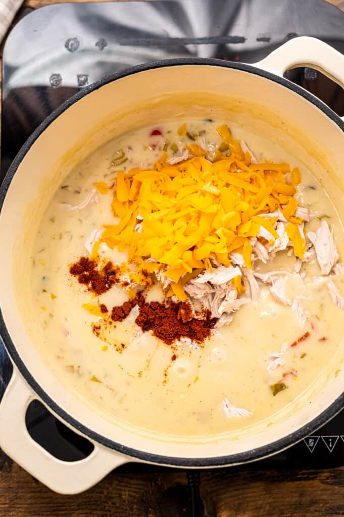 Stock pot with corn chowder and shredded cheese.