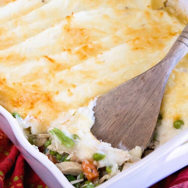 Turkey shepherds pie in a white casserole dish with a wood spatula in it