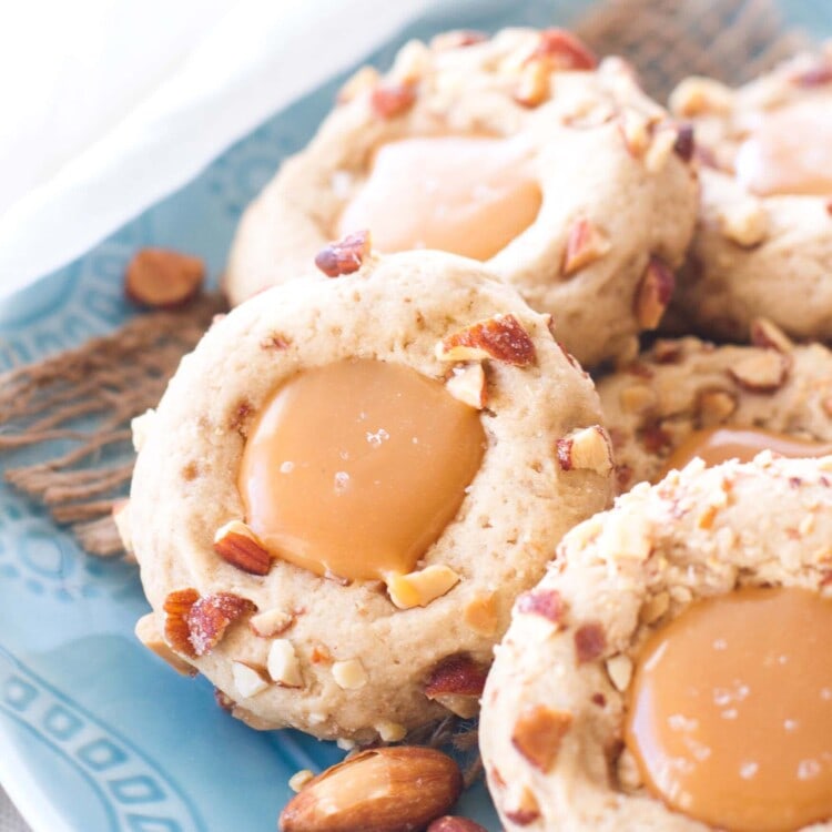 Caramel thumbprint cookies on a blue plate with almonds
