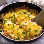 Cheesy bacon and egg hash brown skillet in a pan with a wooden spatula on a white towel