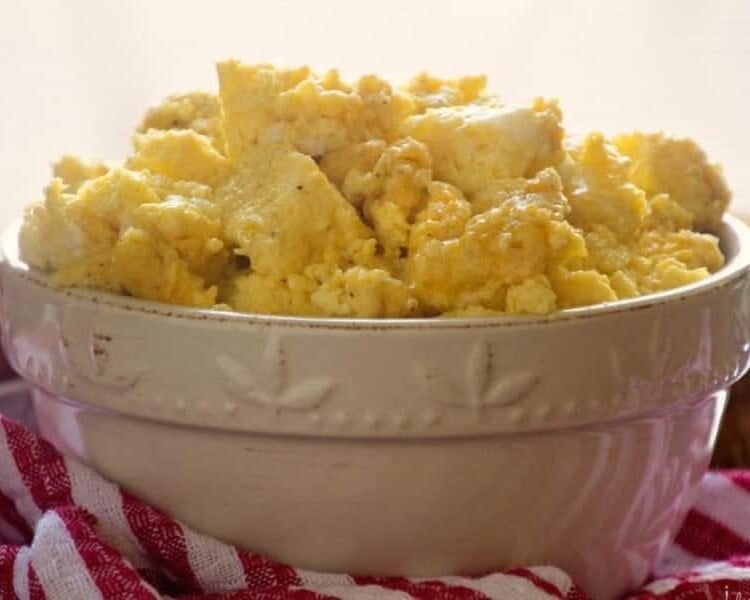 A white bowl of oven baked scrambled eggs sitting on a red and white kitchen towel