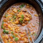 Slow cooker beef and vegetable soup in a black crock pot with a silver ladel