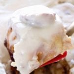 A spatula lifting a sugar cookie cinnamon roll out of a baking dish