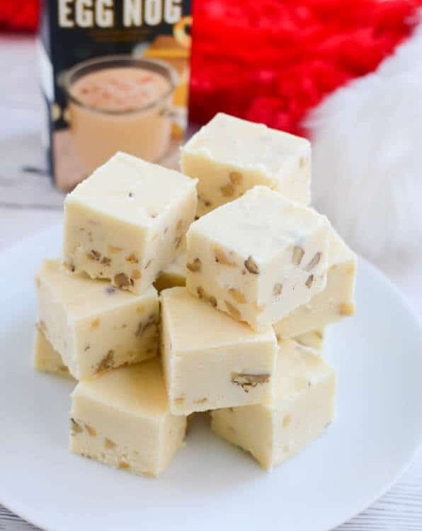Stacks of eggnog fudge on a white plate in front of a Christmas stocking and a carton of egg nog