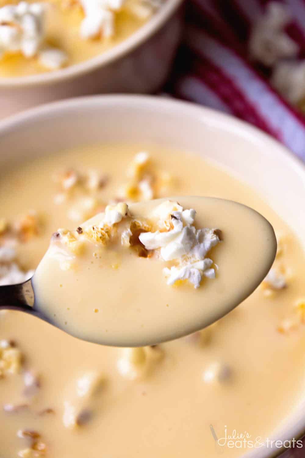 A spoon with beer cheese soup and popcorn on it.