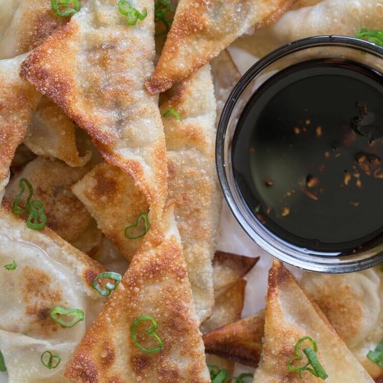 Overhead image of pork potstickers on a white plate with a clear glass bowl of sauce