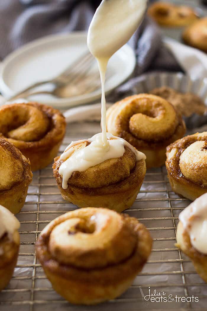 A spoon drizzling icing over the top of the muffins on baking rack.