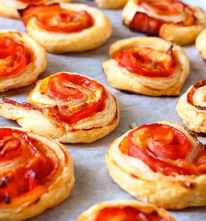 Puff pastry bacon pinwheels with cheddar cheese on parchment paper on a baking sheet