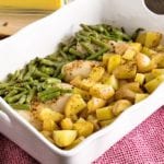 White casserole dish of green beans, chicken, and potatoes sitting on a red kitchen towel