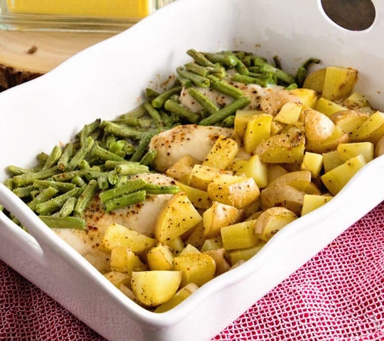White casserole dish of green beans, chicken, and potatoes sitting on a red kitchen towel