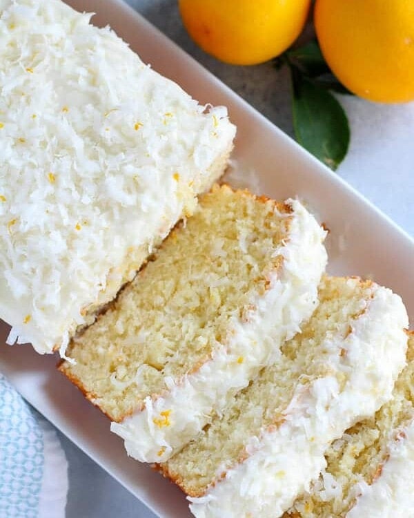 A partially sliced lemon and coconut loaf cake on a white tray