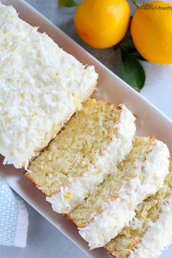 A sliced lemon coconut cake on a white serving platter with lemons in background.