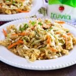 Two white plates loaded with Asian ramen salad on a wood table next to a jar of truvia