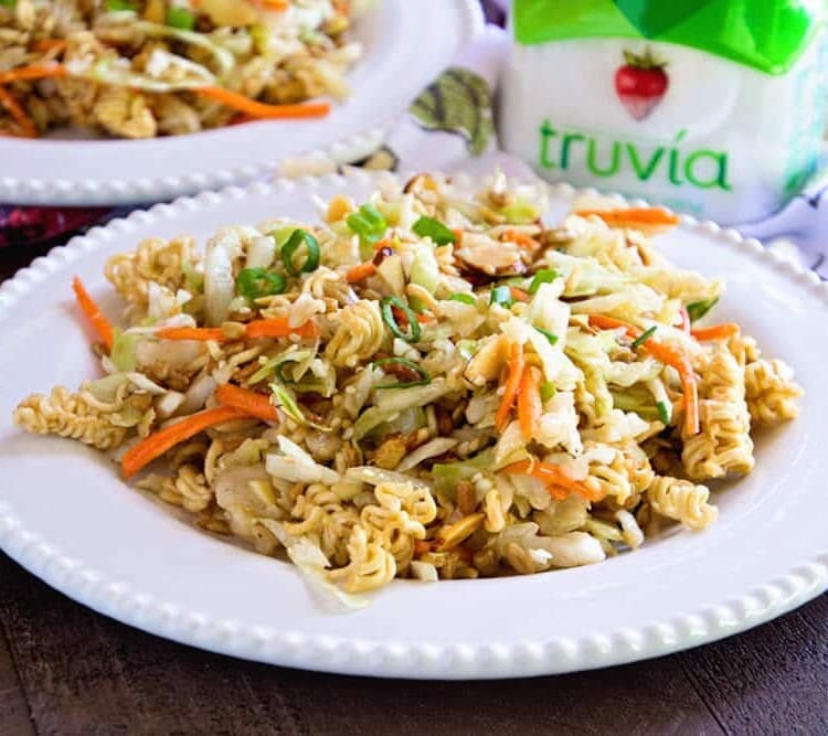 Two white plates loaded with Asian ramen salad on a wood table next to a jar of truvia