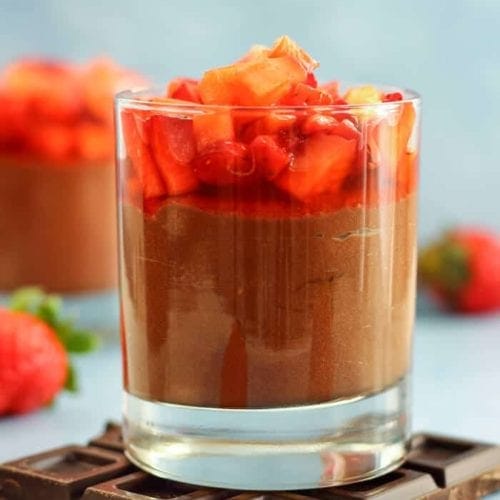 Glass of chocolate nutella mousse topped with strawberries siting on a chocolate bar