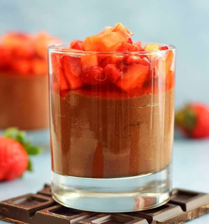 Glass of chocolate nutella mousse topped with strawberries siting on a chocolate bar