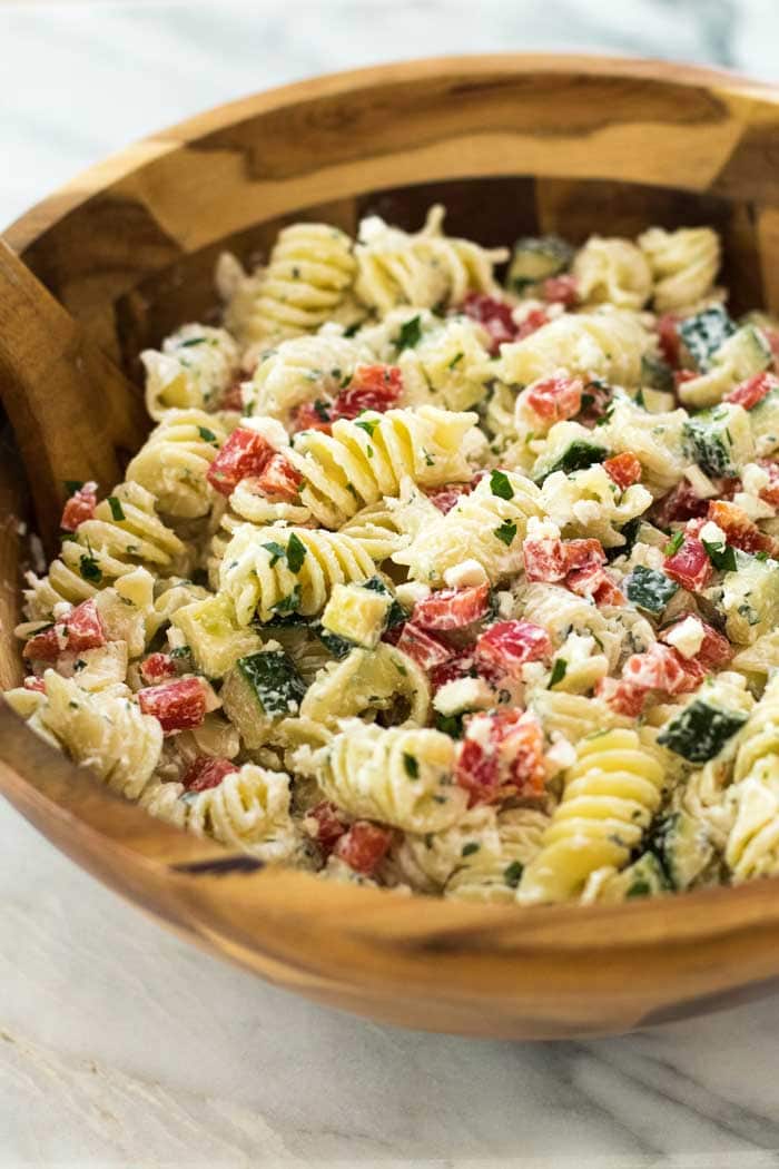 A large wooden bowl filled with Greek Pasta Salad on a marble background