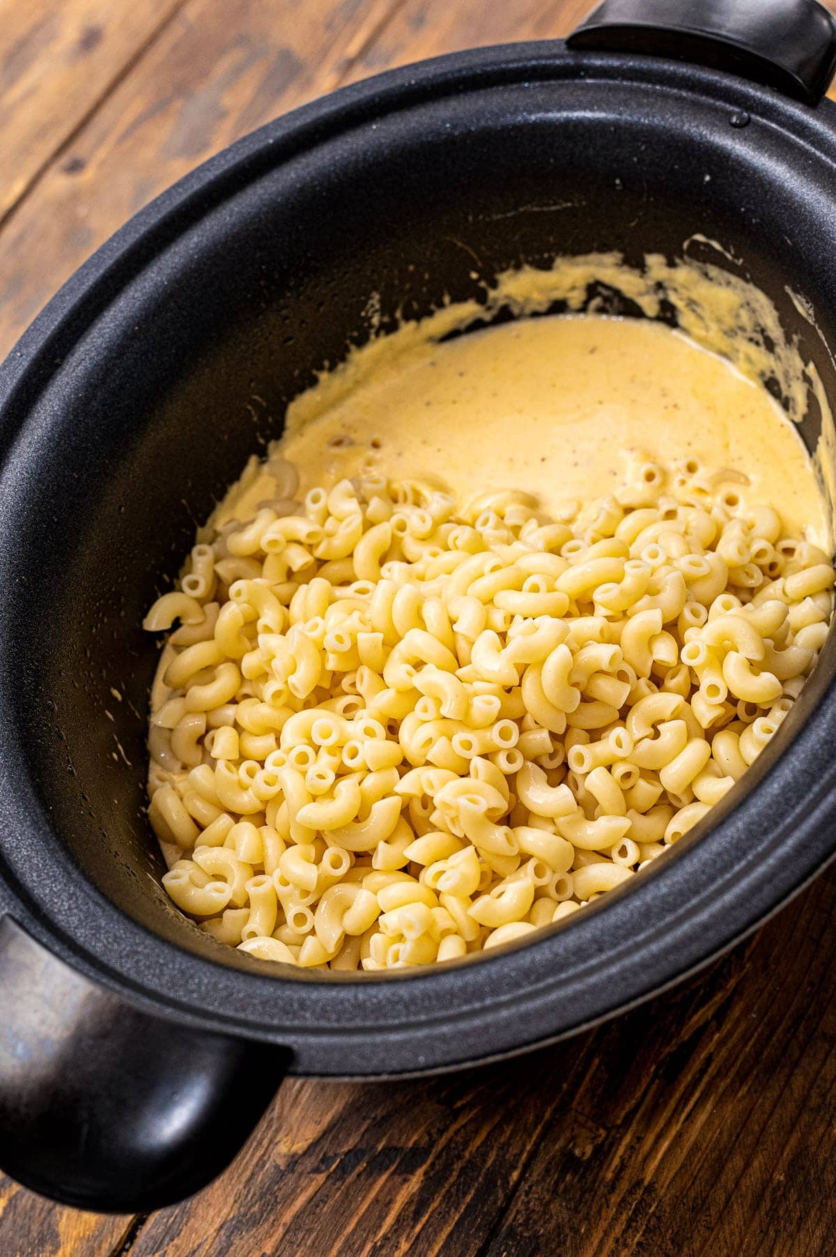 Slow Cooker with cheese sauce and cooked macaroni noodles before mixing