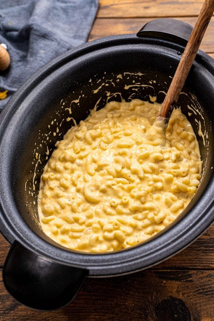 Wooden spoon sitting in a slow cooker full of mac and cheese.