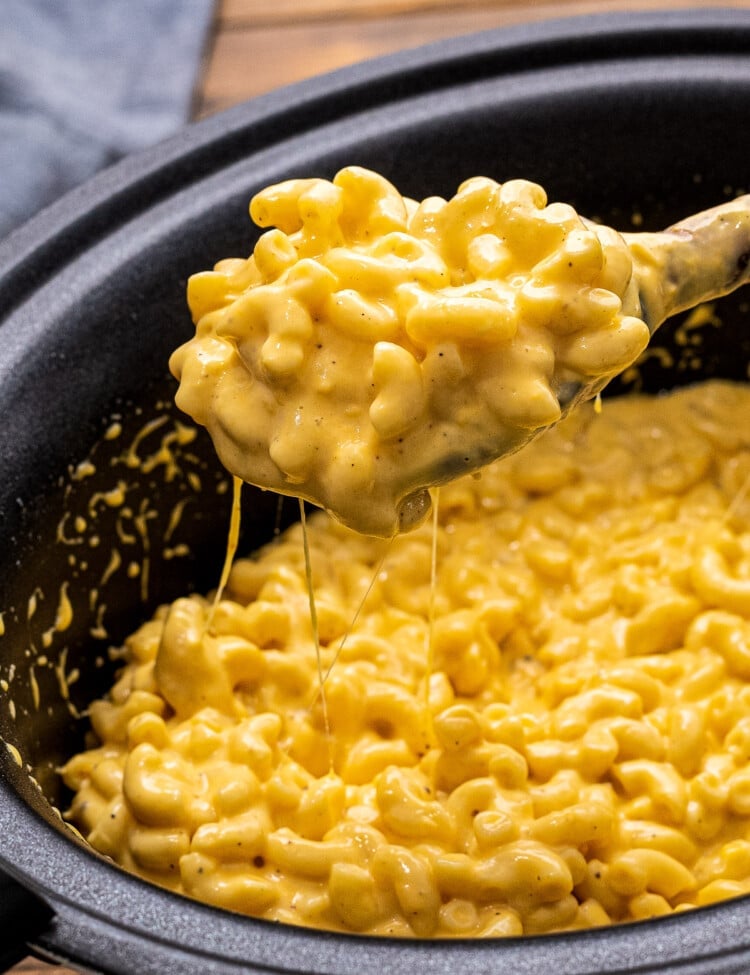 Slow Cooker Mac and Cheese being scooped out of slow cooker with wooden spoon