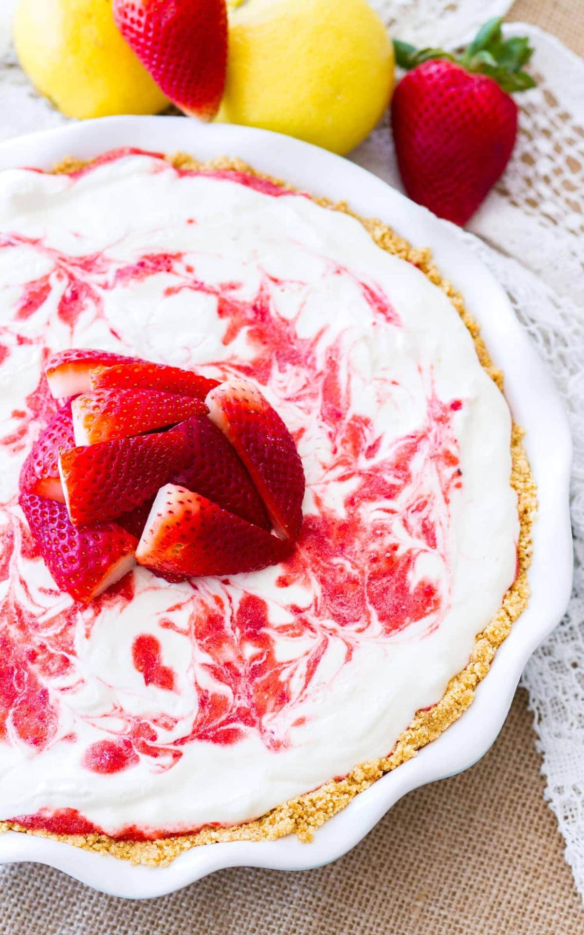 An overhead picture of Frozen Lemonade Pie in a white pie tin surrounded by strawberries and lemons. Strawberry lemonade icebox pie is a perfect no-bake dessert for summer!