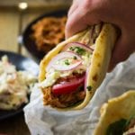 Hand holding a bbq pulled pork gyro over a basked lined with parchment paper