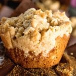 Up close image of a crumb banana muffin sitting on a brown paper muffin liner