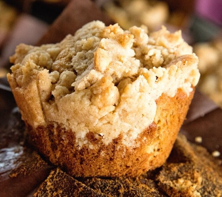 Up close image of a crumb banana muffin sitting on a brown paper muffin liner