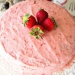 Easy fresh strawberry cake sitting on a white cake stand topped with four whole strawberries