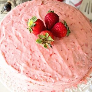 Easy fresh strawberry cake sitting on a white cake stand topped with four whole strawberries