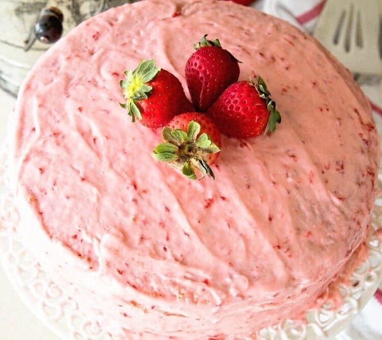 Easy fresh strawberry cake sitting on a white cake stand topped with four whole strawberries