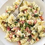 Overhead image of greek pasta salad in a white bowl with a fork