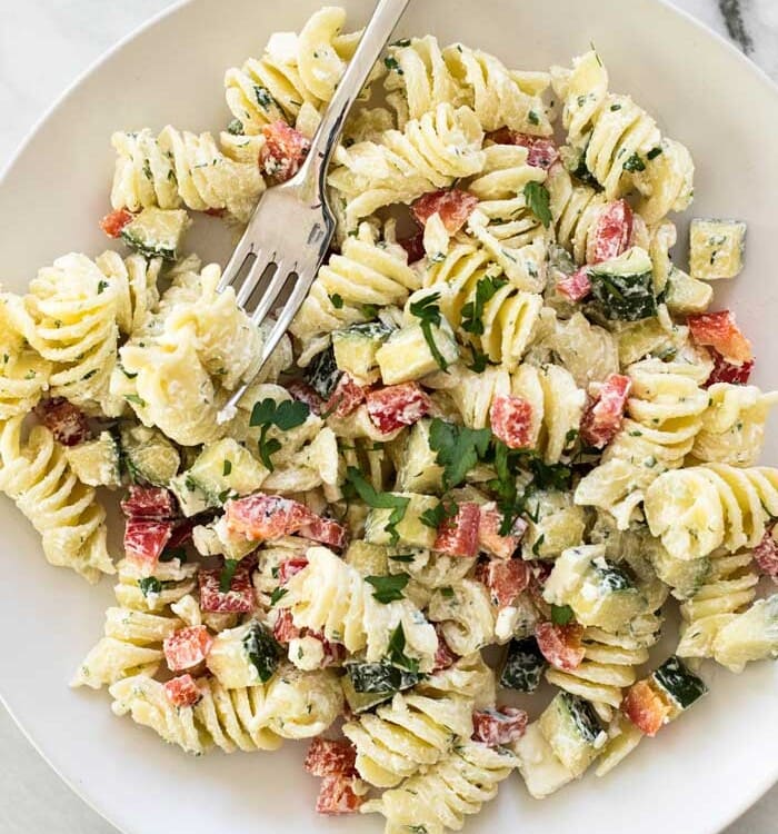 Overhead image of greek pasta salad in a white bowl with a fork