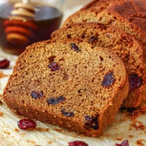 Slices of honey cranberry bread on a table with a glass jar of honey