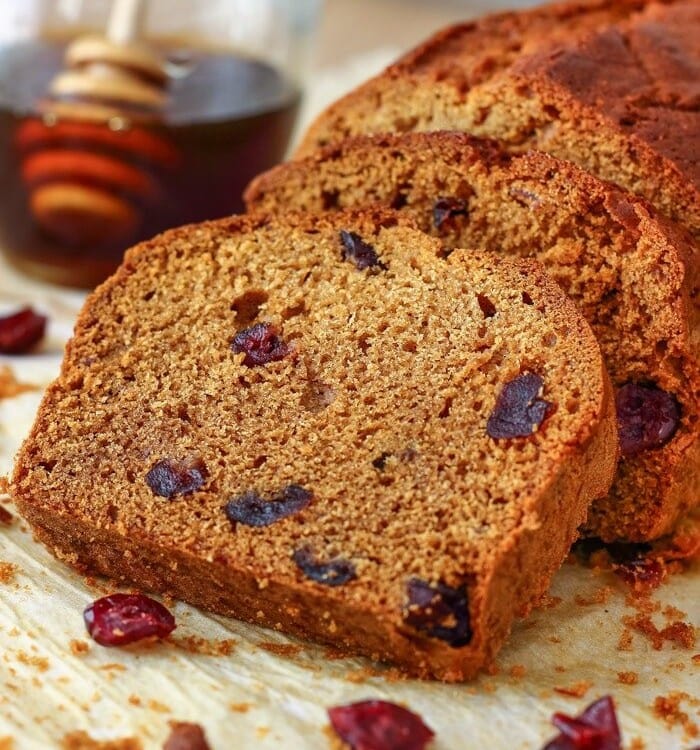 Slices of honey cranberry bread on a table with a glass jar of honey