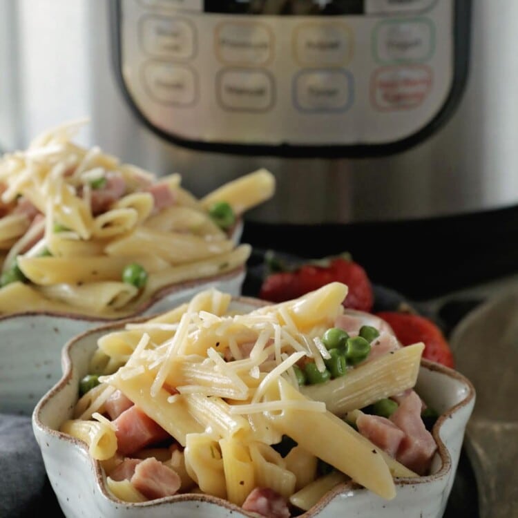 Two bowls of ham and penne pasta with shredded parmesan cheese sprinkled over the top