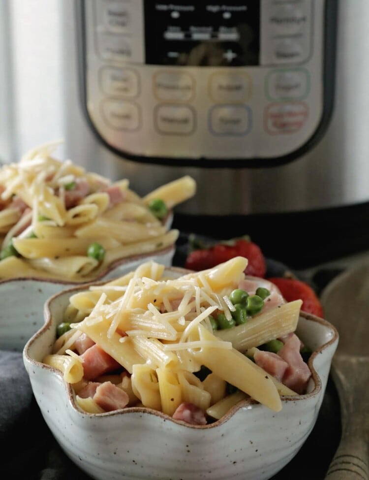 Two bowls of ham and penne pasta with shredded parmesan cheese sprinkled over the top