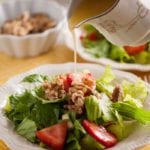 Strawberry romaine salad in a white bowl with dressing being poured over the top