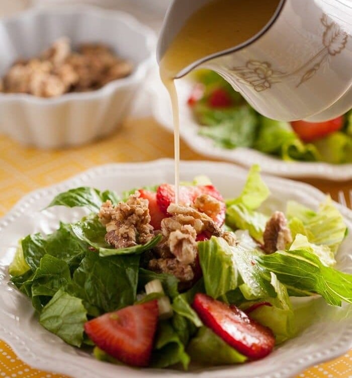 Strawberry romaine salad in a white bowl with dressing being poured over the top