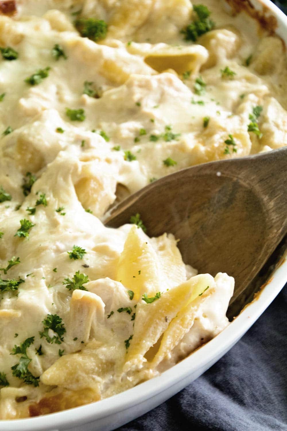 Unstuffed Chicken Alfredo Shells in a white serving bowl with a wooden spoon 