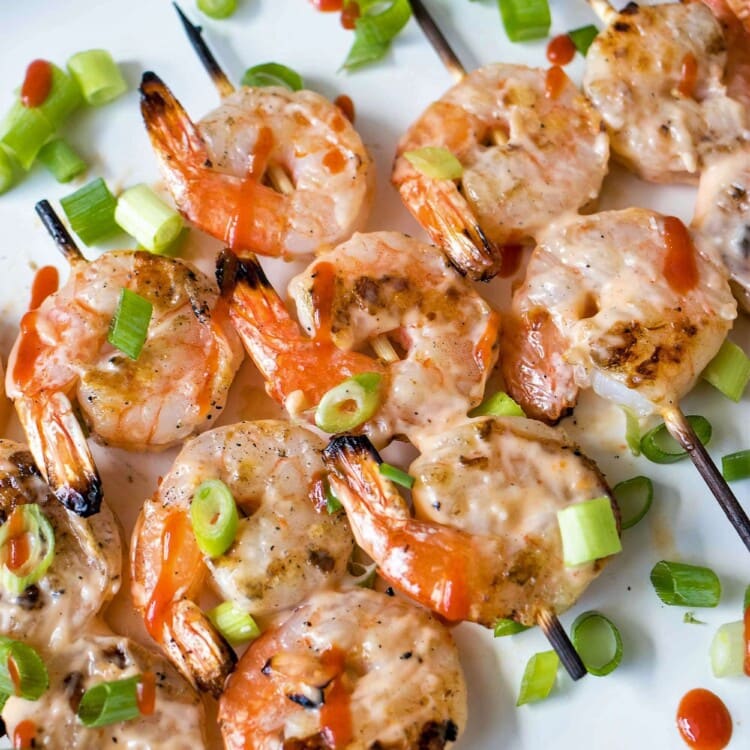 five Grilled Bang Bang Shrimp Skewers white chives on a white plate