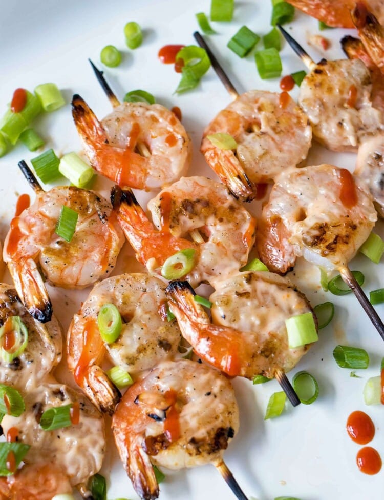 five Grilled Bang Bang Shrimp Skewers white chives on a white plate