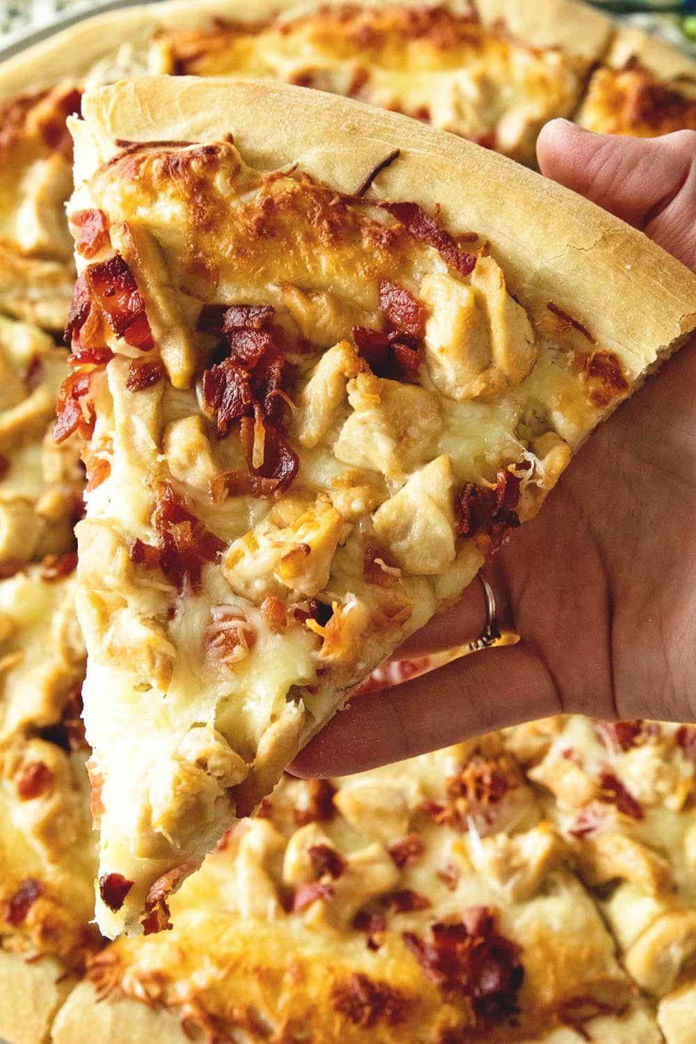 Hand holding a slice of chicken bacon ranch pizza