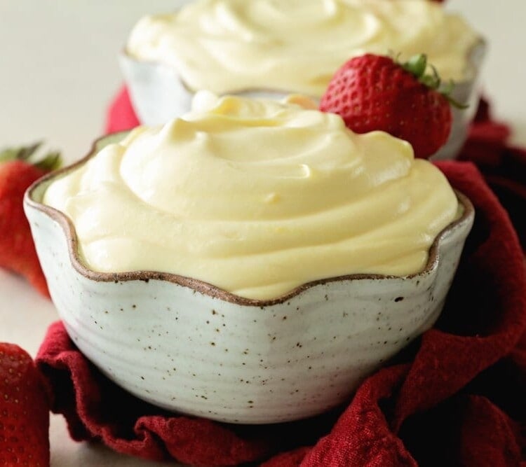 Two cream bowls of easy vanilla pudding with strawberries on a red kitchen towel