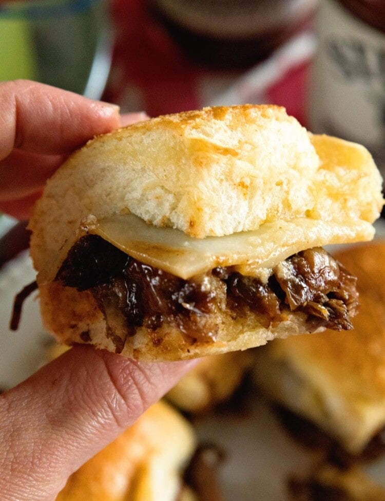 A hand holding a brisket slider with caramelized onions