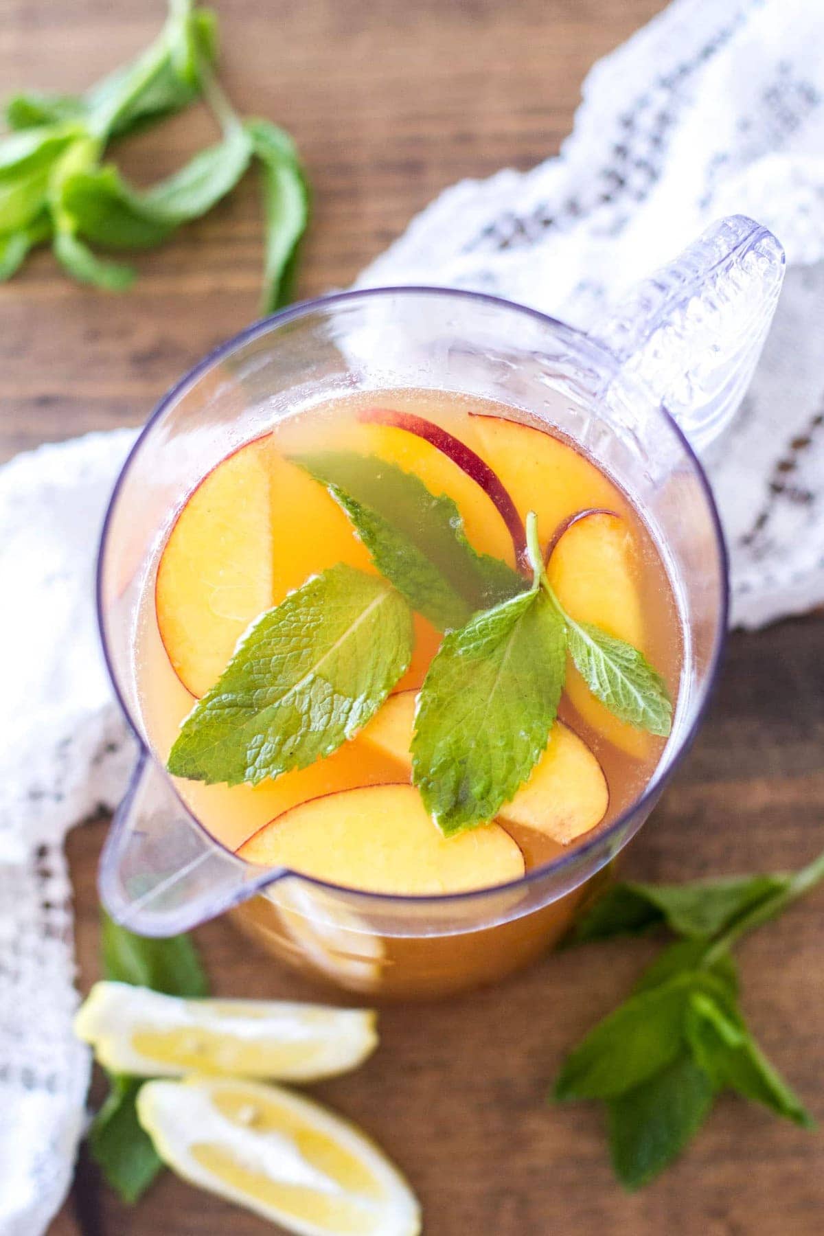 Overhead image of a pitched of iced peach green tea with fresh peaches, mint leaves in the tea. 