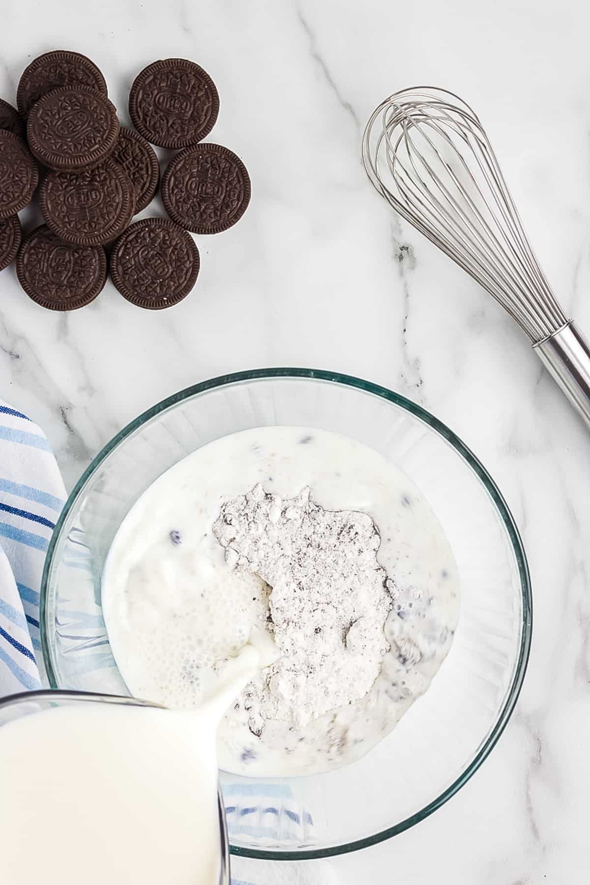 Pouring milk into a glass bowl with cookies 'n creme pudding mix