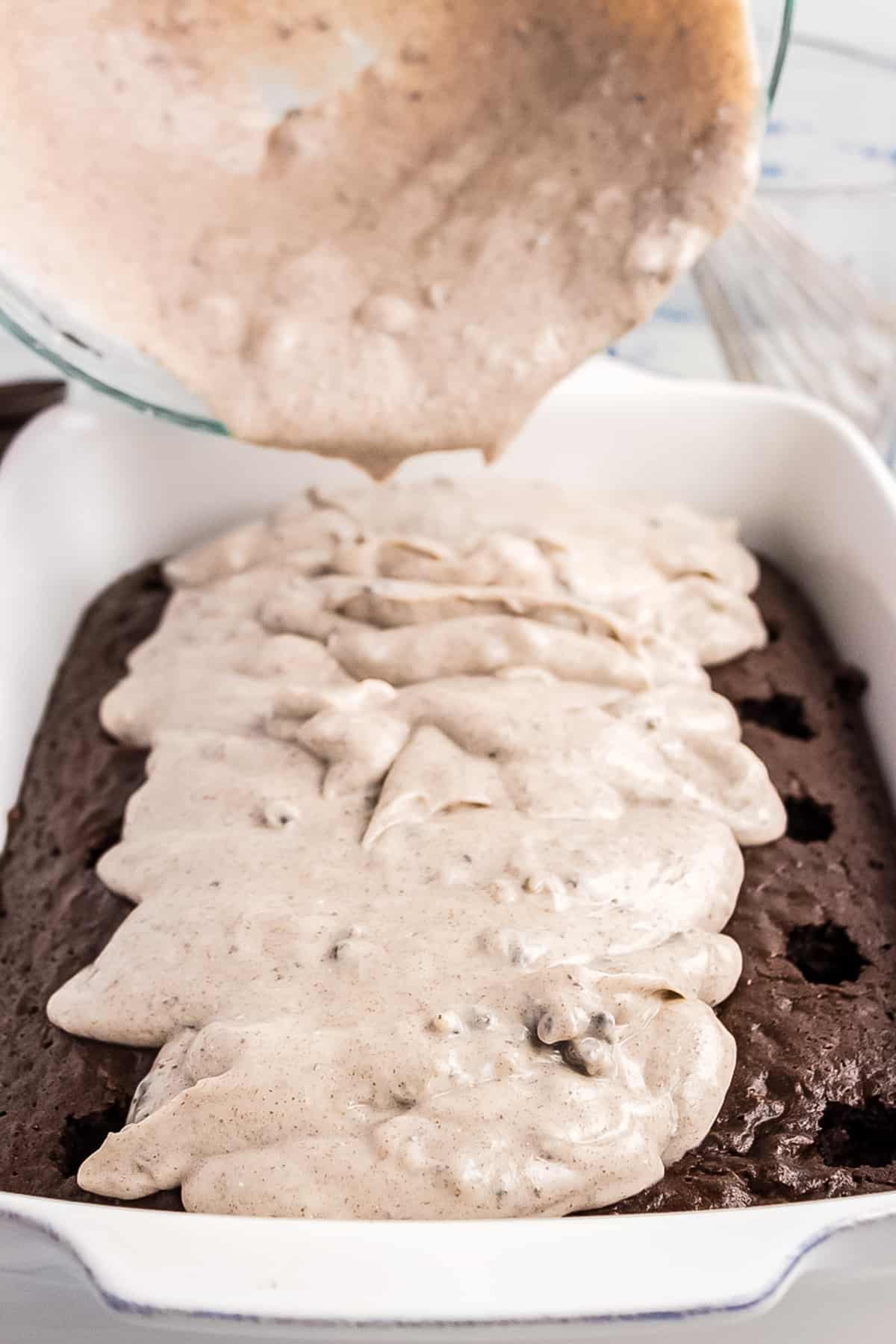 Pouring oreo pudding over the top of chocolate poke cake